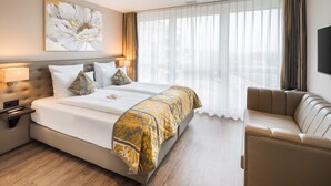 A hotel room with a large bed, a sofa, a flat-screen TV, and a window with sheer curtains. - Hotel Swiss Star (Wetzikon)