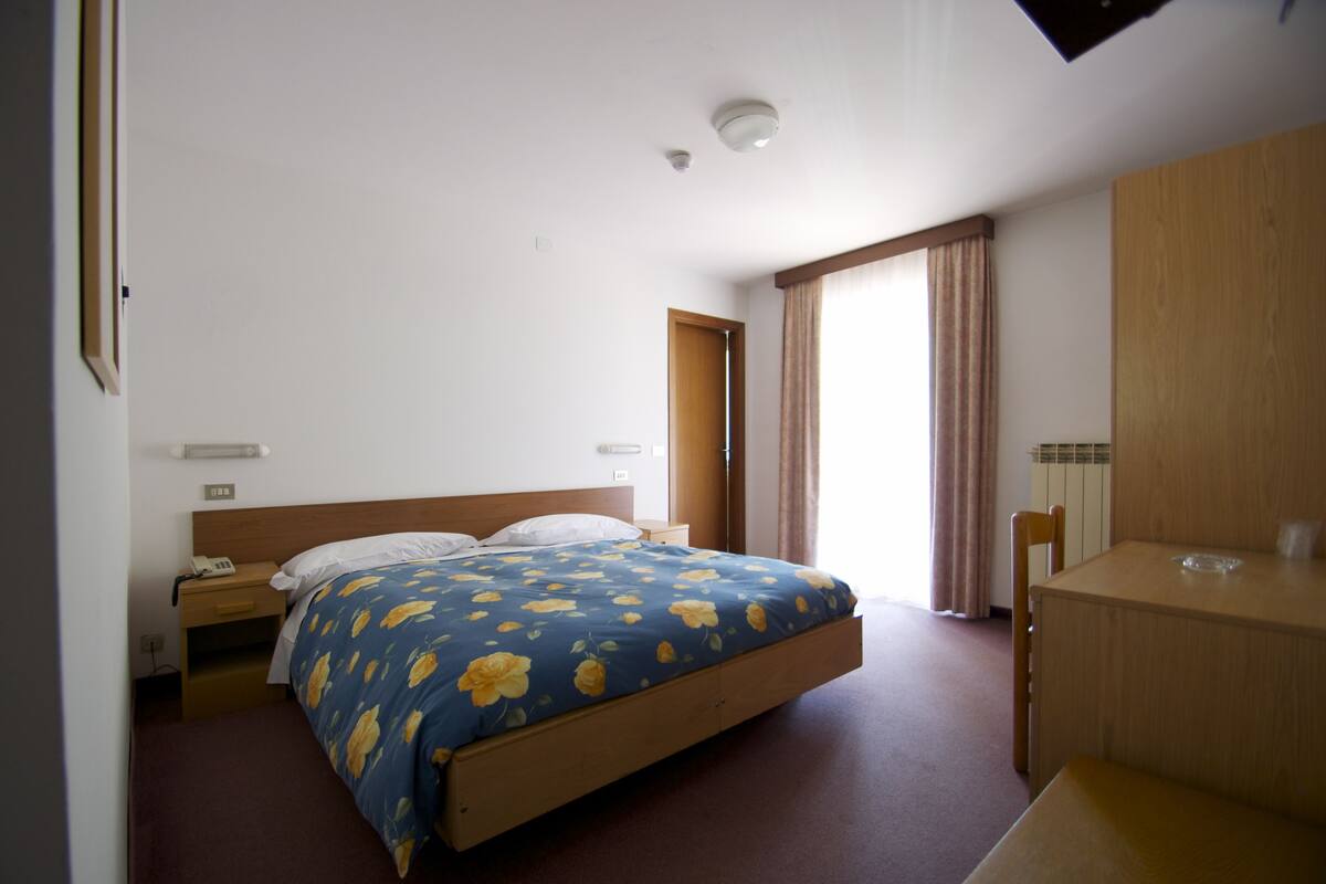 A bedroom with a bed, a wooden nightstand, a desk, and a chair.