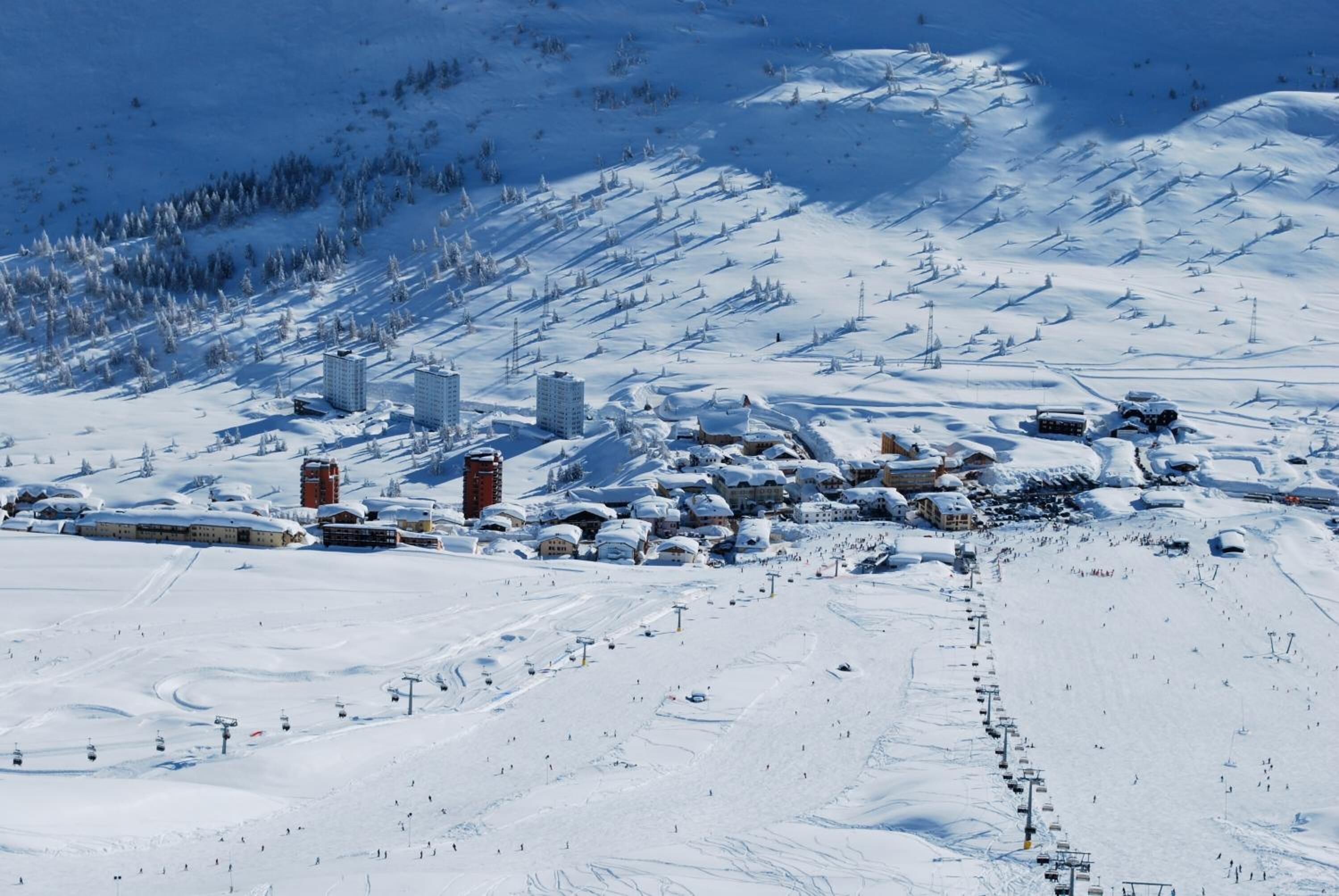 Estación de esquí cubierta de nieve con varios edificios, remontes y una pista de esquí despejada.