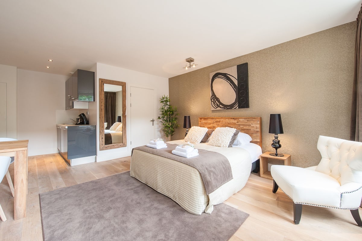 Una habitación de hotel moderna con una cama grande, mesitas de noche, un escritorio y una kitchenette.
