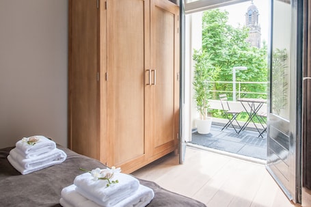 A room with a wooden wardrobe, a glass door leading to an outdoor area with a table and chairs, and towels on a bench.