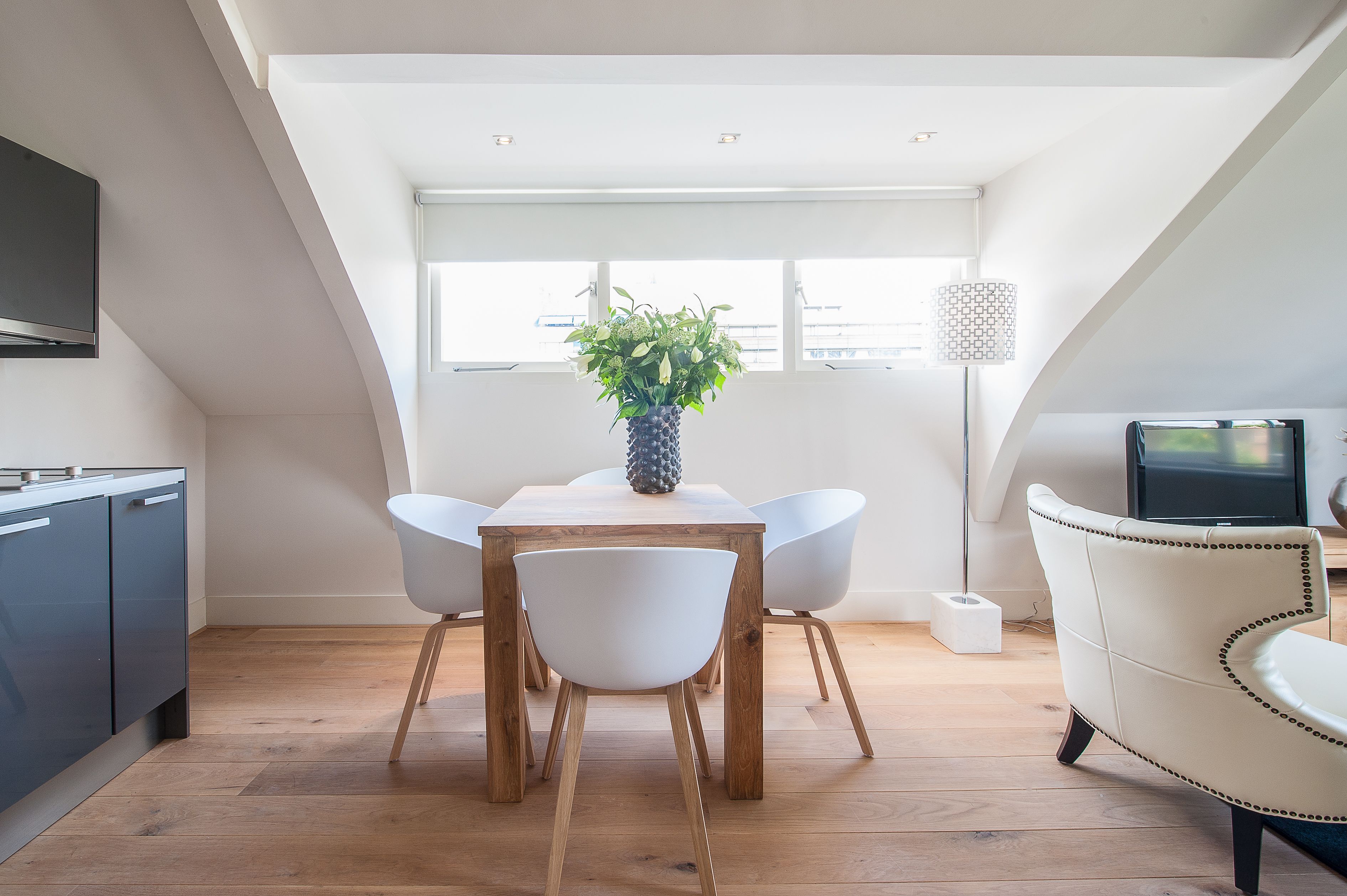 Een moderne eetruimte met een houten tafel, witte stoelen en een potplant.