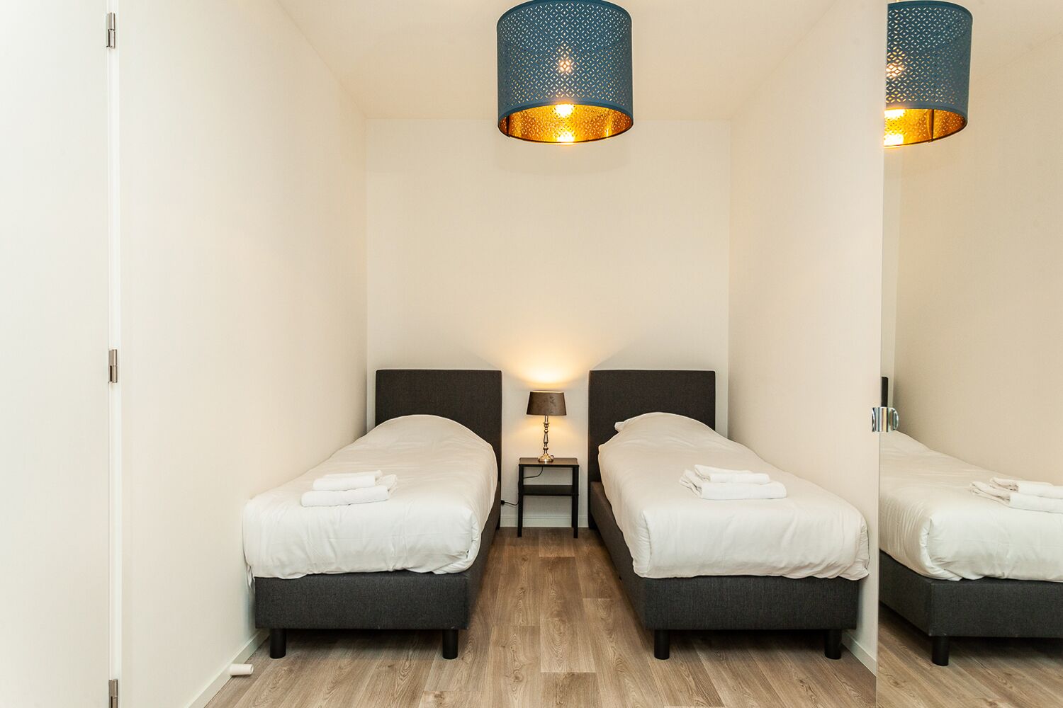 Een hotelkamer met twee enkele bedden, een nachtkastje met een lamp en een spiegel.