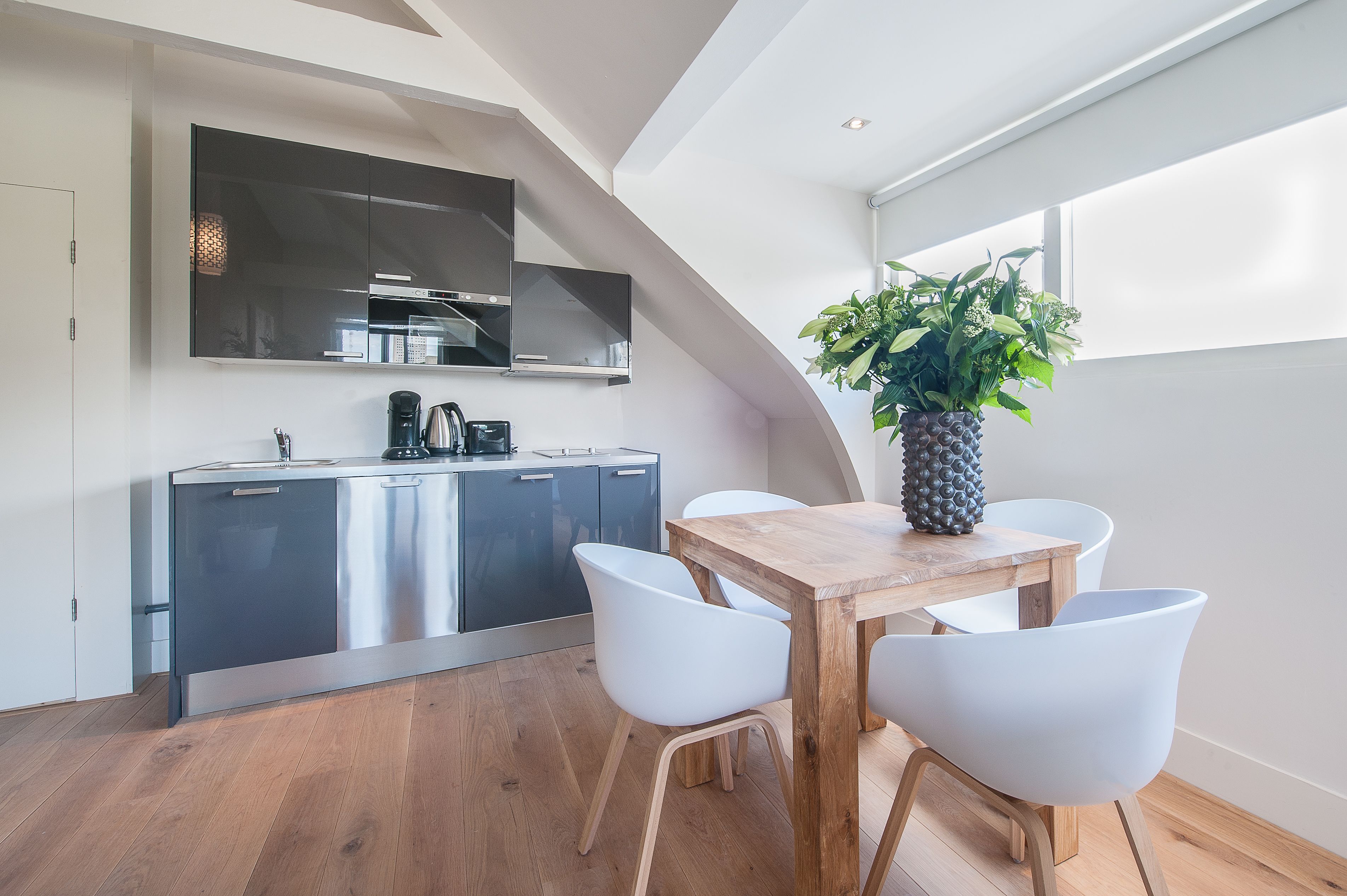 Una cucina moderna con mobili scuri, un tavolo da pranzo in legno e sedie bianche.