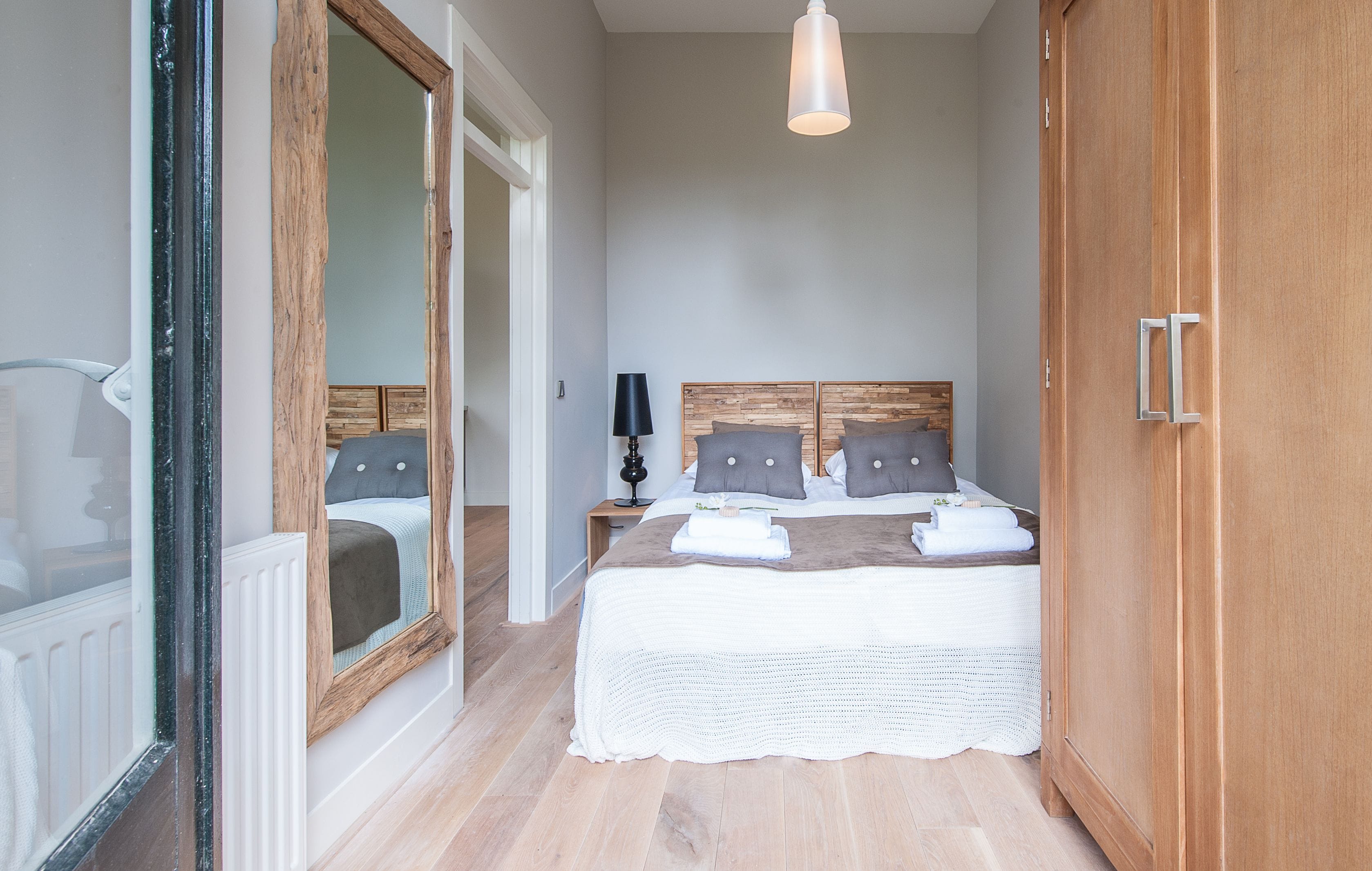 Un dormitorio con una cama grande, cabecera de madera, una mesita de noche con lámpara y un armario.