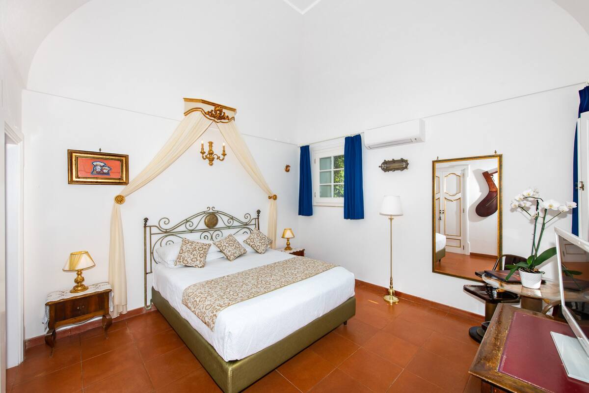 A bedroom with a bed, bedside tables, a mirror, and a desk with a computer.