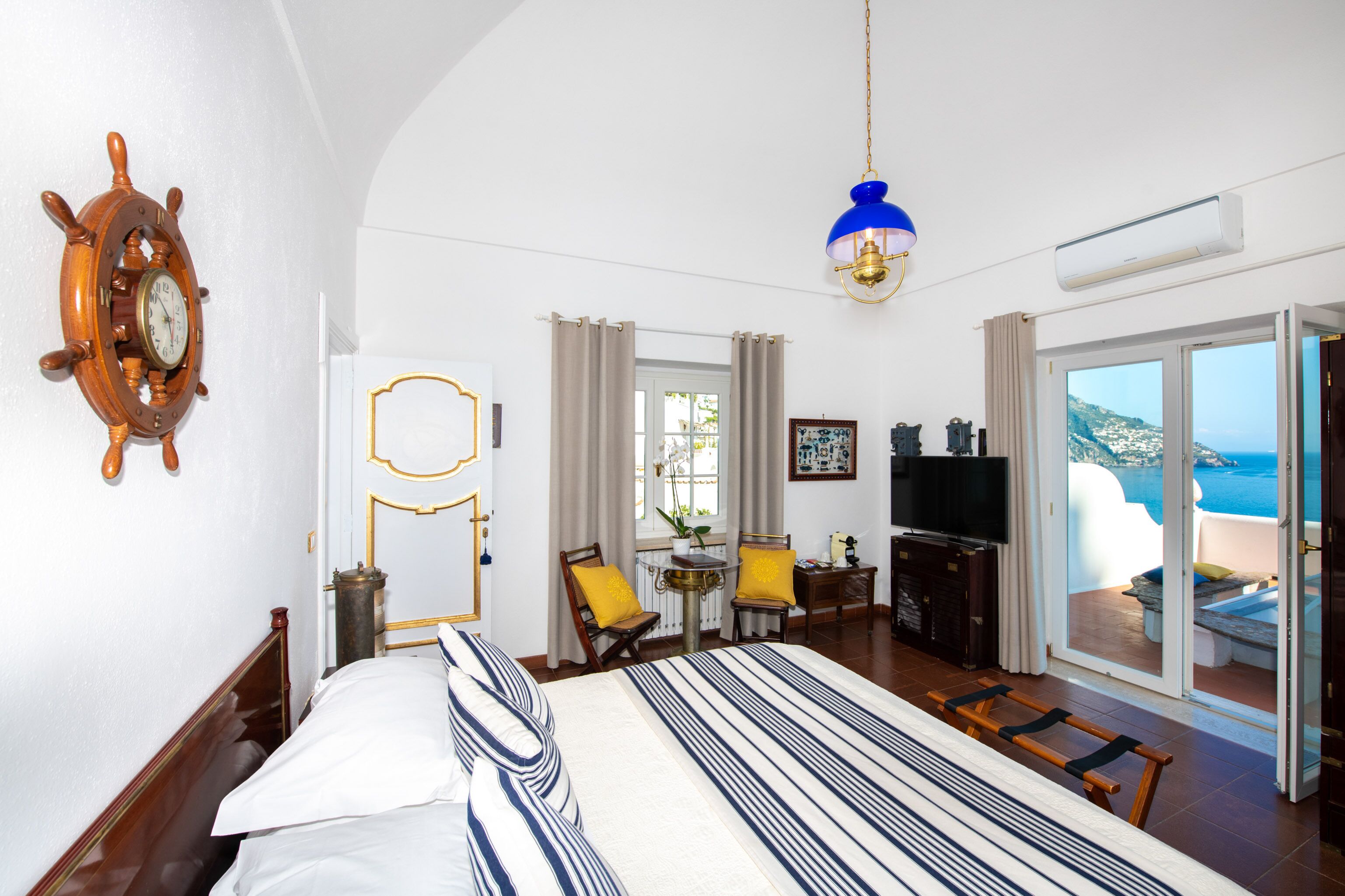 A hotel room with a bed, a desk, a television, and a view of the sea.