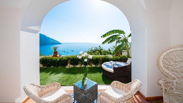 Une chambre avec vue sur la mer, des meubles en osier et une petite table surmontée d’un vase.
