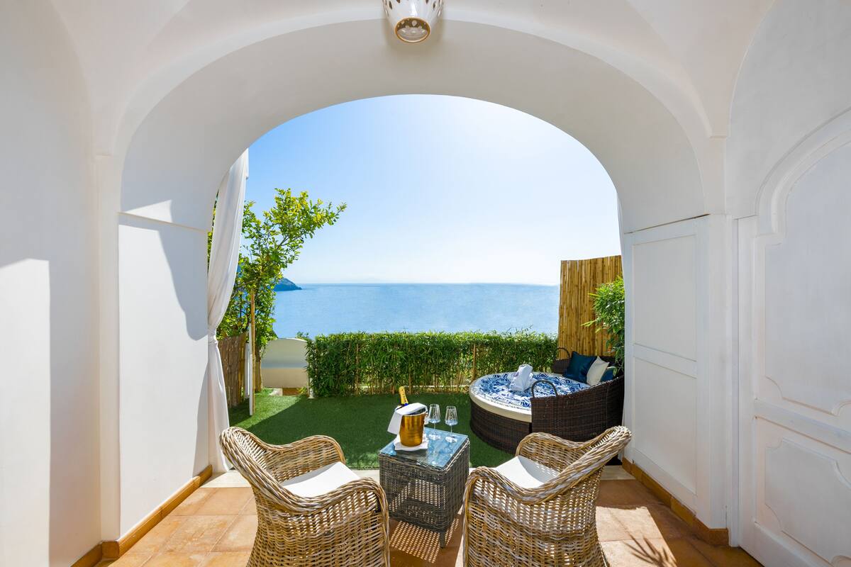 A balcony with wicker furniture, a hot tub, and a view of the sea.