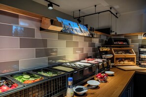 A buffet area with various food options, a coffee machine, and a display case with bread. - mk | hotel berlin (Berlin)