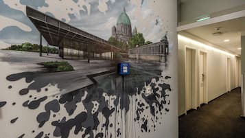 Un pasillo con un mural de un puente y un edificio, un buzón azul y piso alfombrado.