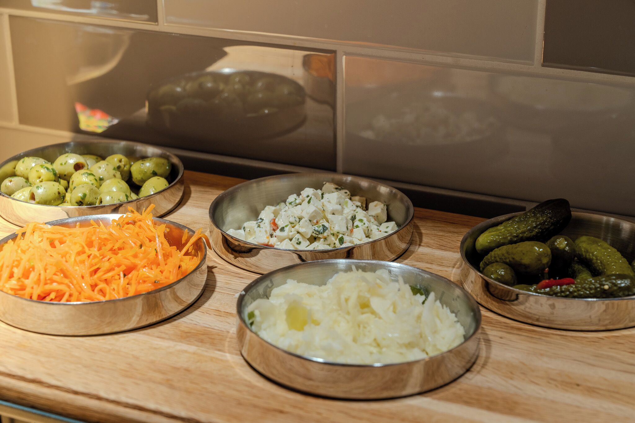 A kitchen counter with various food items in bowls, including shredded carrots, chopped onions, and pickles.