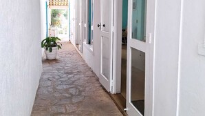 A narrow corridor with white walls and doors, a potted plant, and a stone floor. - Pousada Mar de Búzios (Búzios)