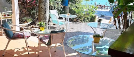 An outdoor patio with wicker furniture, a glass table, and a view of the sea.