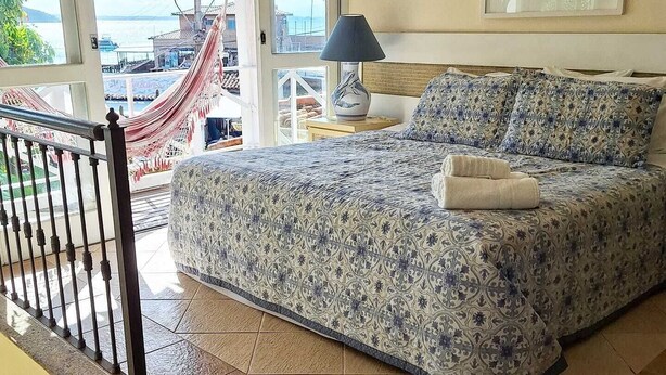 A bedroom with a bed, a nightstand, a lamp, and a view of the outside. - Pousada Mar de Búzios (Búzios)