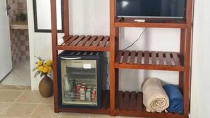 Una habitación con un mueble bajo de televisión de madera, un refrigerador pequeño y un estante con una toalla enrollada.