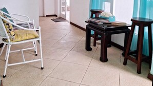 Amplia sala de estar con una silla blanca, una mesita con libros y una cortina azul.