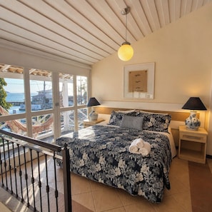 A bedroom with a large bed, two bedside lamps, a framed artwork on the wall, and a view of the sea through large windows. - Pousada Mar de Búzios (Búzios)