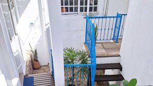 Una escalera con barandas azules que lleva a una plataforma, rodeada de paredes blancas y plantas en macetas.