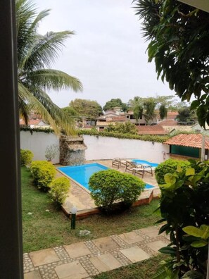 A residential area with a swimming pool, a stone wall, and a view of neighboring houses. - Pousada Areias Brancas (Búzios)