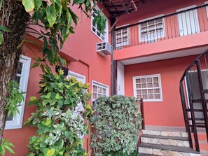 A red building with a balcony, a staircase, and a small garden area. - Pousada Areias Brancas (Búzios)
