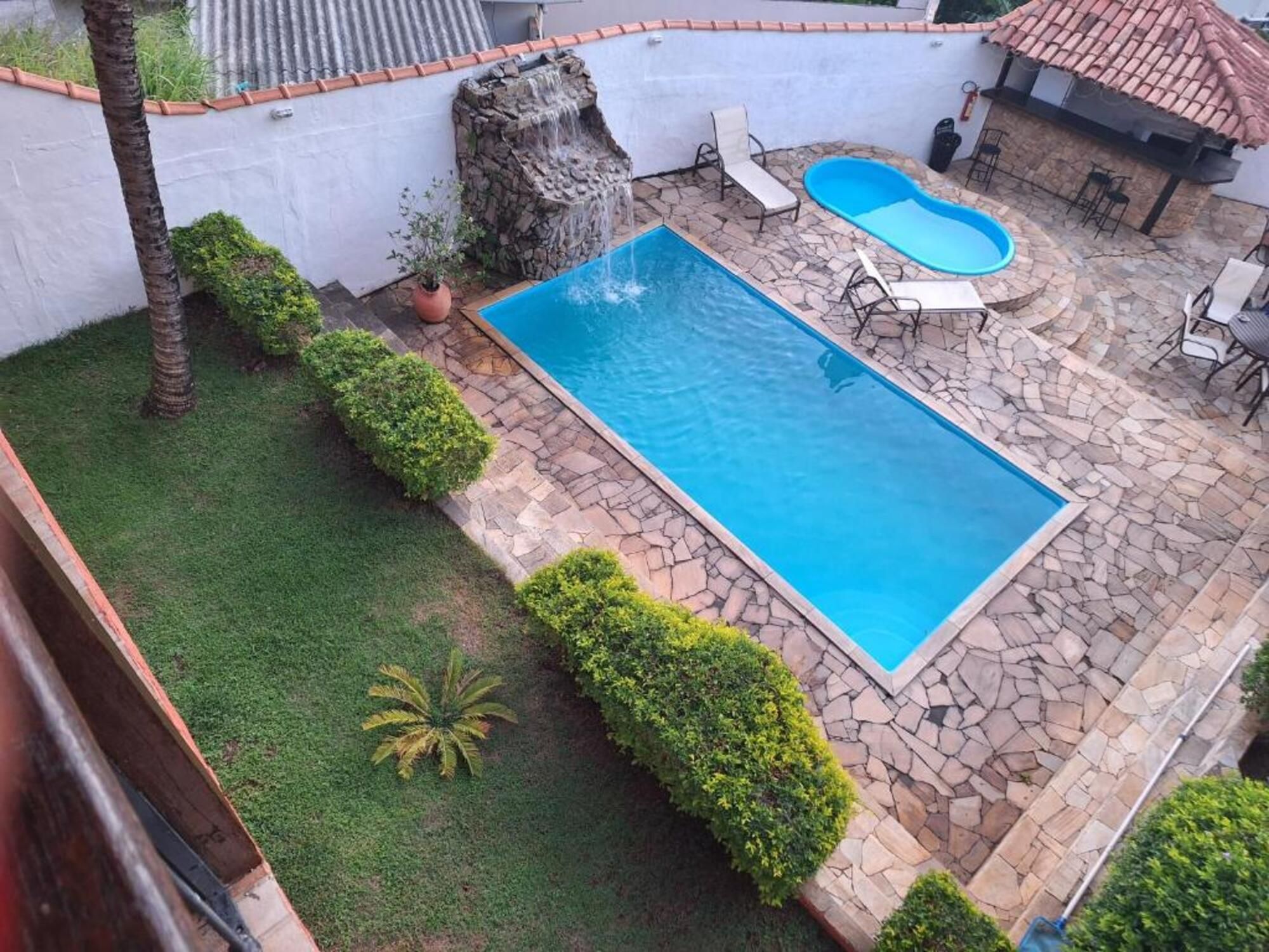 Una piscina rectangular con borde de piedra, rodeada de césped y unos pocos arbustos.