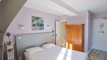 Une chambre à coucher comprenant un lit, un radiateur, une armoire en bois, une porte et une lampe fixée au mur.