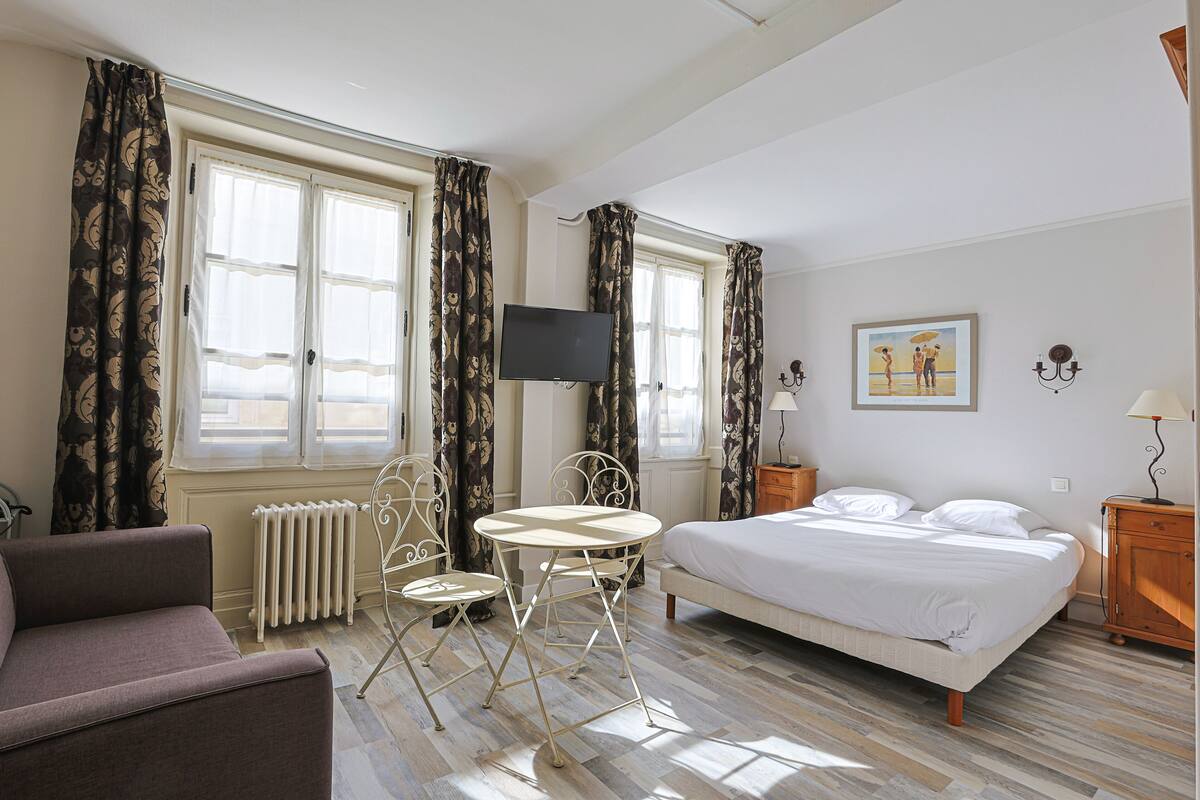 A hotel room with a bed, a sofa, a table with chairs, a TV, and a radiator.