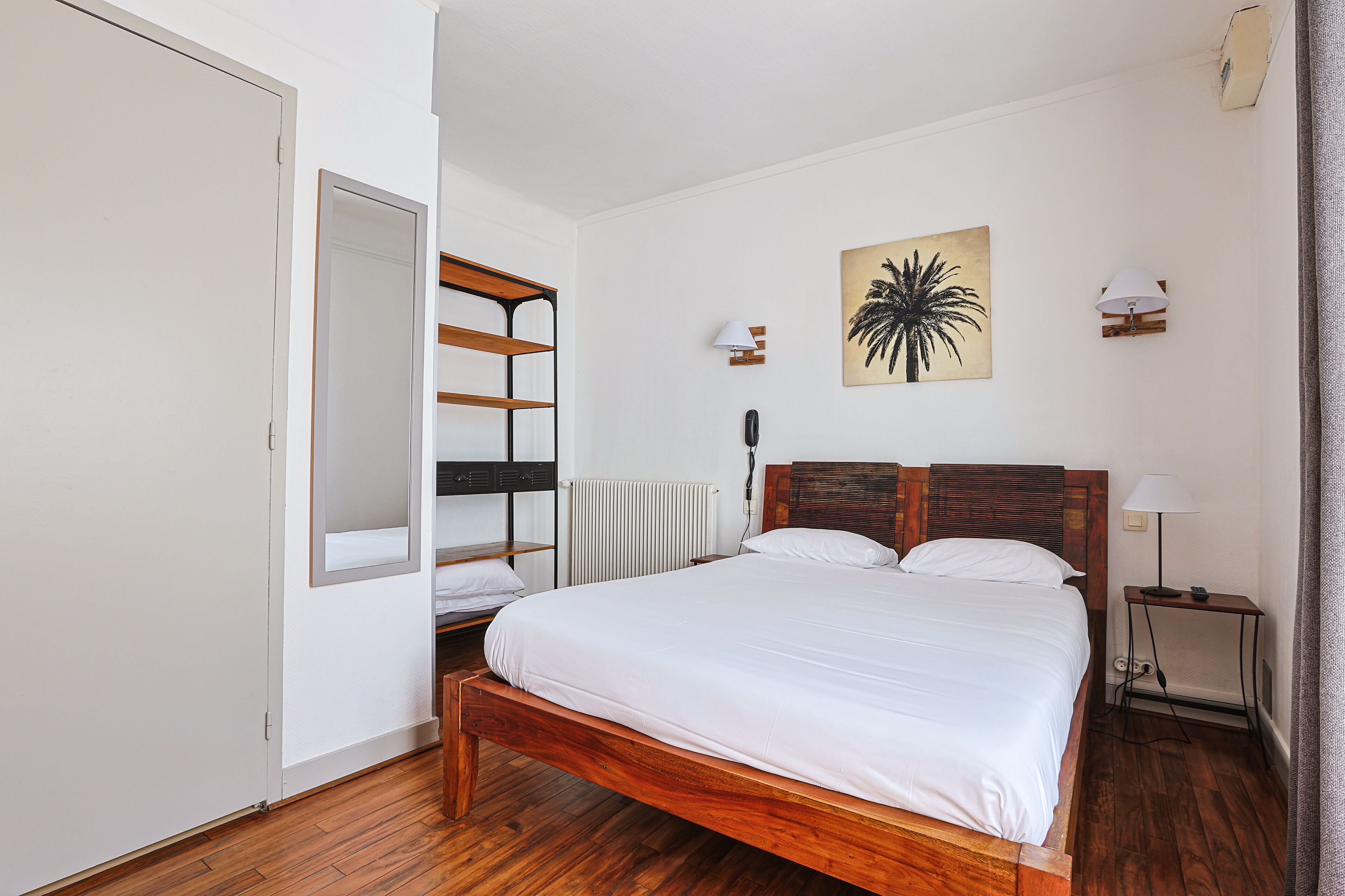 Un dormitorio con una cama de madera, un radiador, una lámpara de pared y un cuadro.