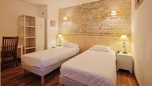 Una habitación con dos camas individuales, un armario de madera, un escritorio y una silla.