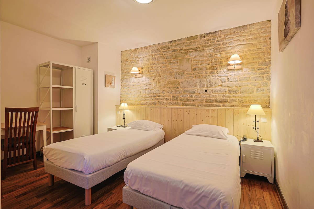 A room with two single beds, a wooden wardrobe, a desk, and a chair.