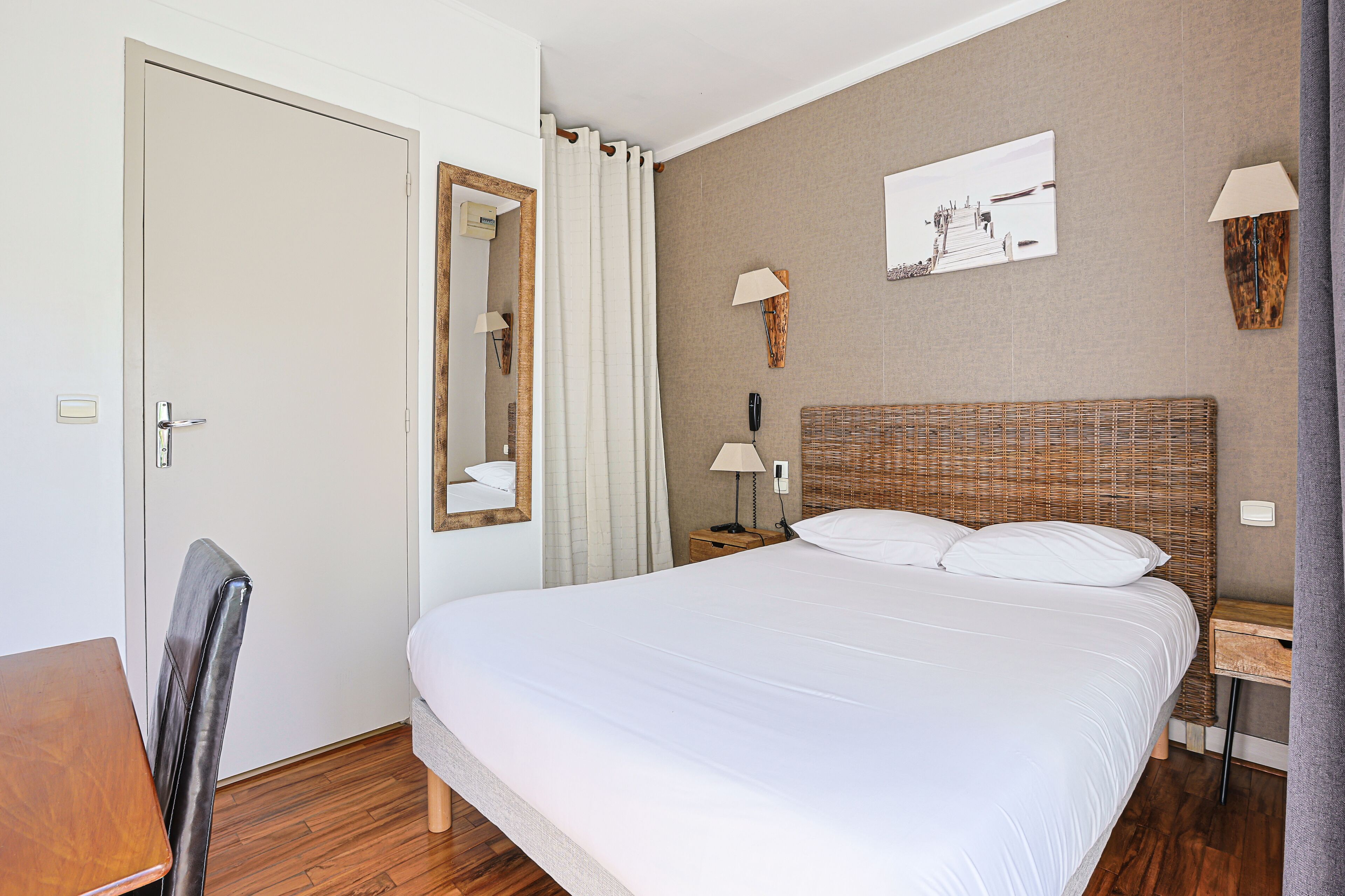 Une chambre d’hôtel bien aménagée, avec un grand lit, un bureau en bois, une chaise, un miroir et deux tables de chevet équipées de lampes.