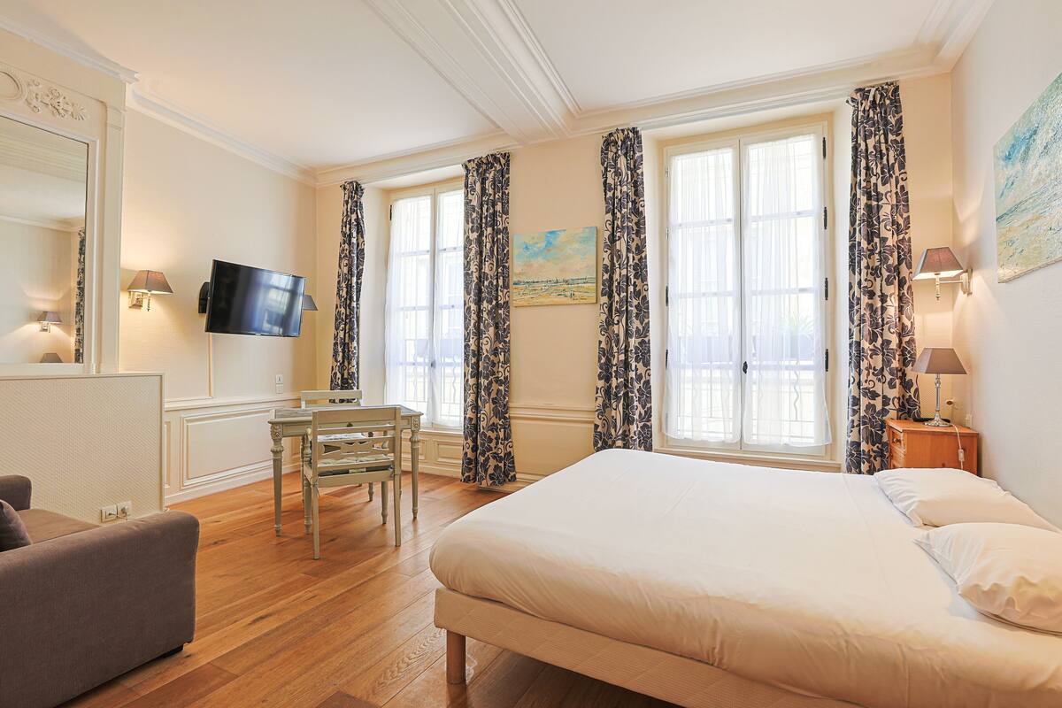 A hotel room with a large bed, a desk with a chair, a television, and a painting on the wall.