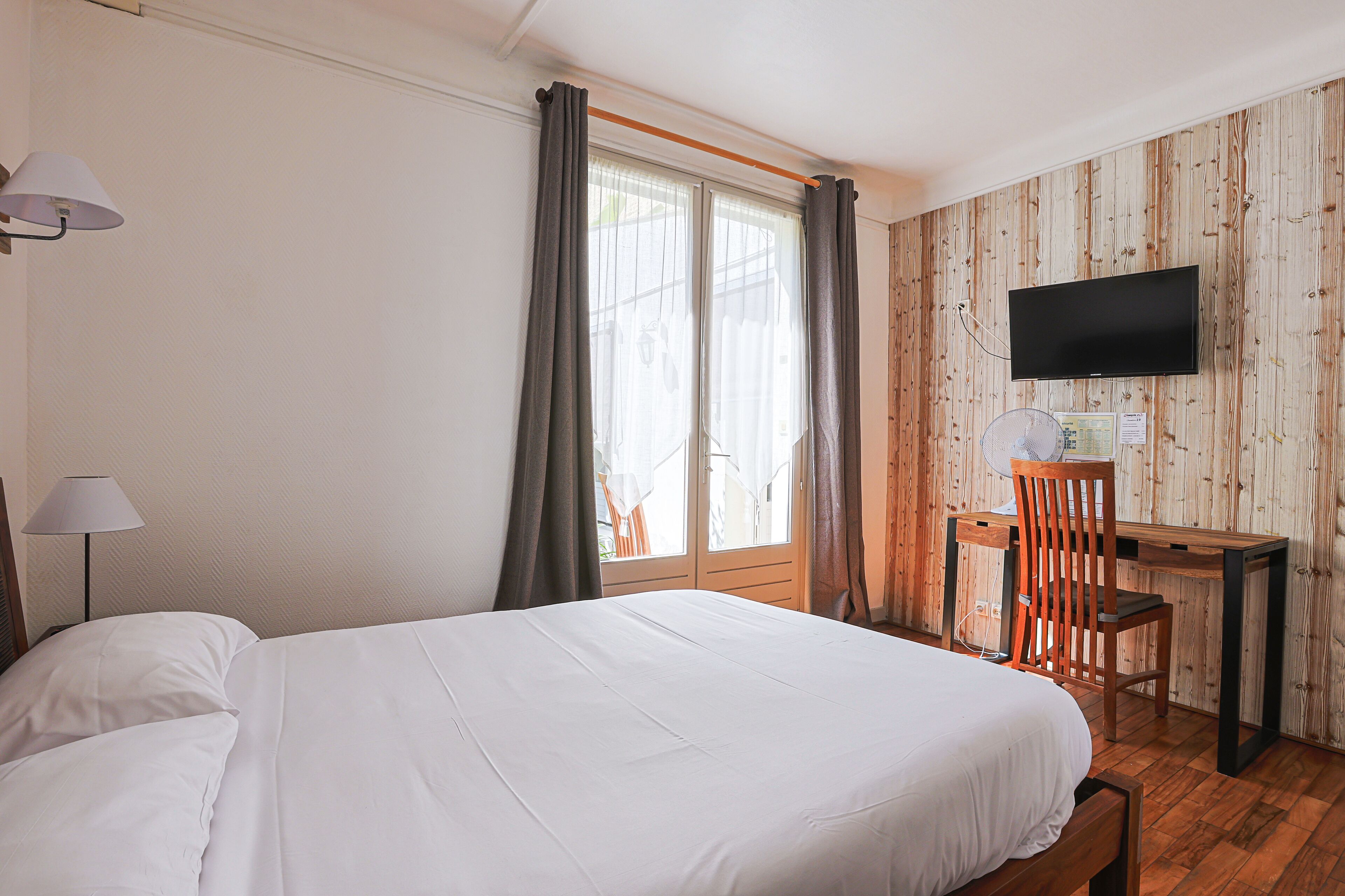 A hotel room with a bed, a desk, a chair, a TV, and a window with curtains.
