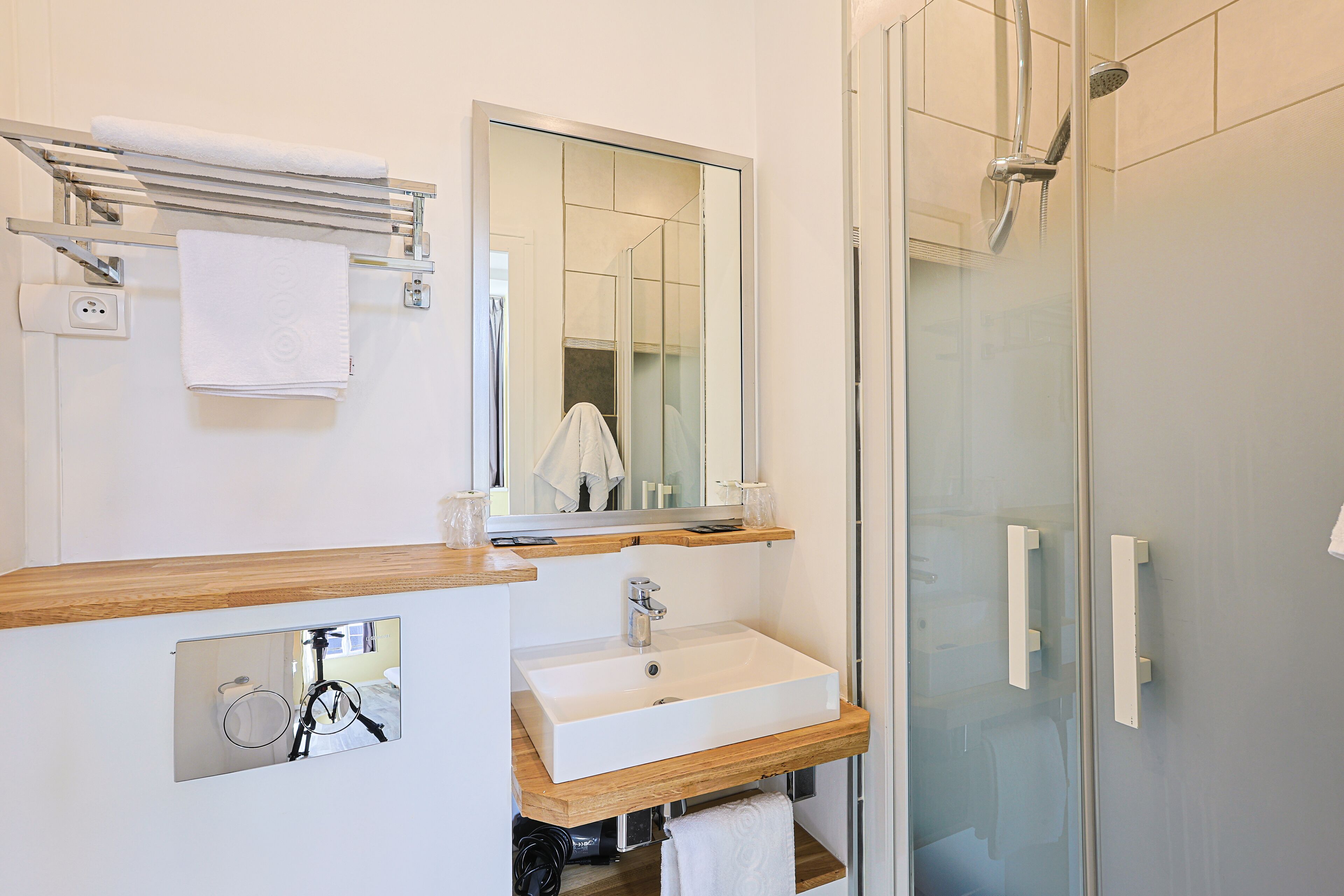 Een moderne badkamer met een douchecabine van glas, een witte wastafel en een spiegel erboven.