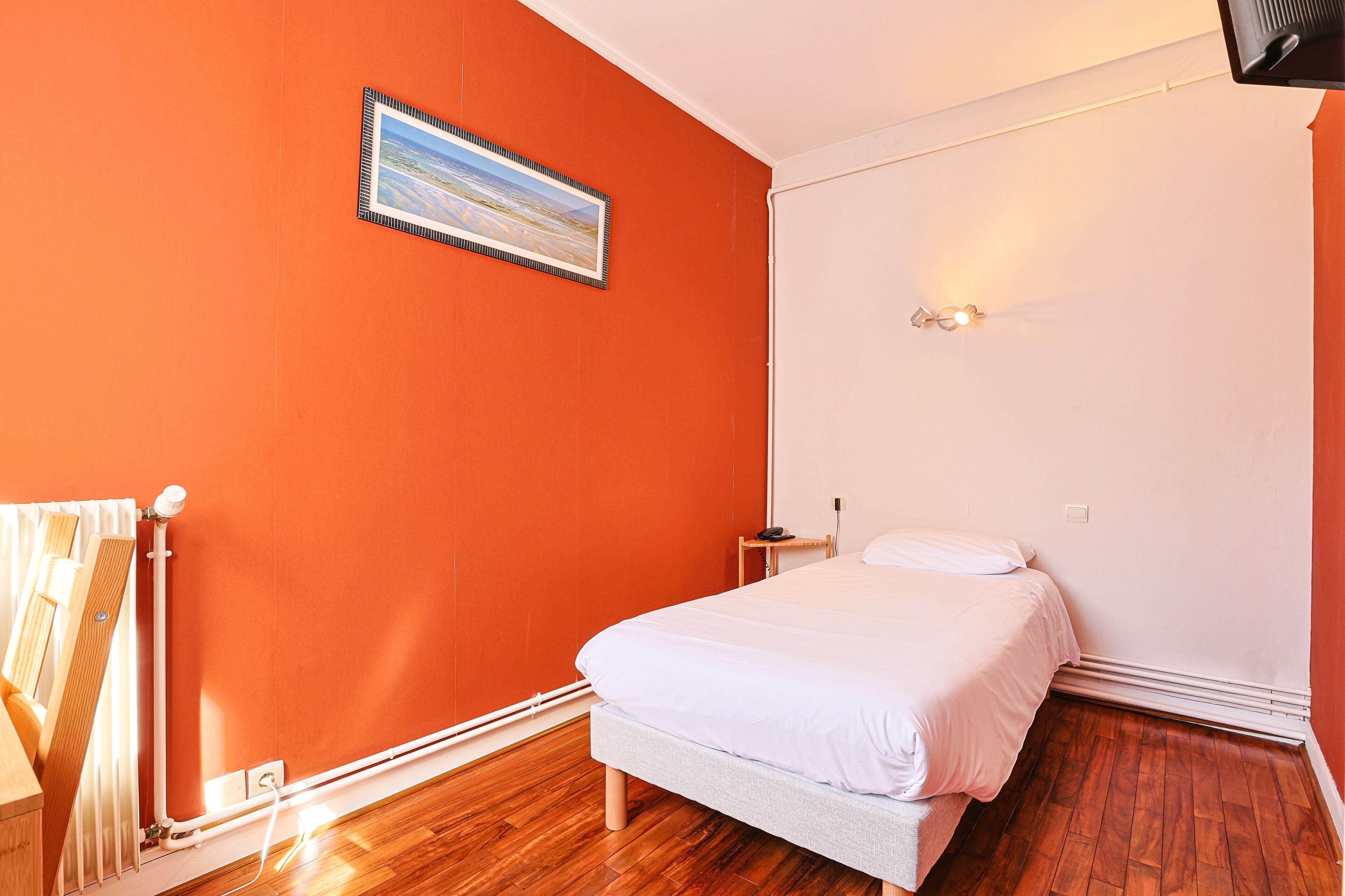 Un dormitorio con una pared naranja, una cama, una mesita de noche y un cuadro.
