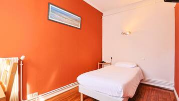 Un dormitorio con una pared naranja, una cama, una mesita de noche y un cuadro.