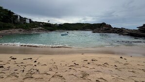 A beach with clear water, a boat, and rocky outcrops. - Pousada Sereia de Geriba (Búzios)