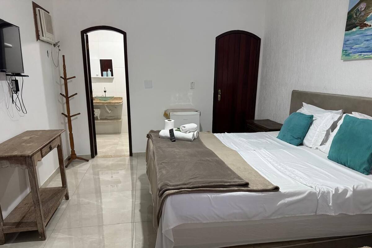 Un dormitorio con cama, mesita de noche, armario y baño visible a través de una puerta abierta.