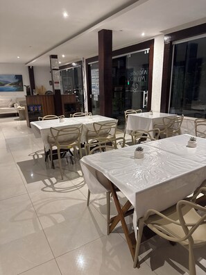 Un restaurante con varias mesas y sillas, piso de baldosas y ventanas grandes.