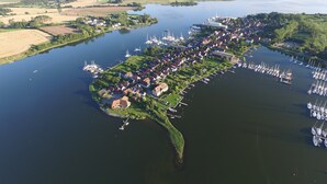 An aerial view of a riverside town with a marina, houses, and fields.