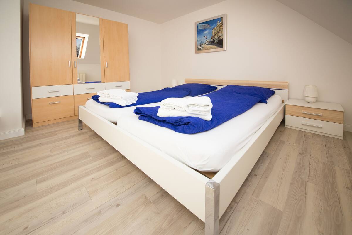 Un dormitorio ordenado con una cama, un armario, una mesita de noche y un cuadro en la pared.