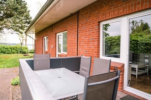 Un espace patio avec une table et des chaises en métal, un mur en briques et une porte-fenêtre coulissante donnant sur un espace de détente extérieur.