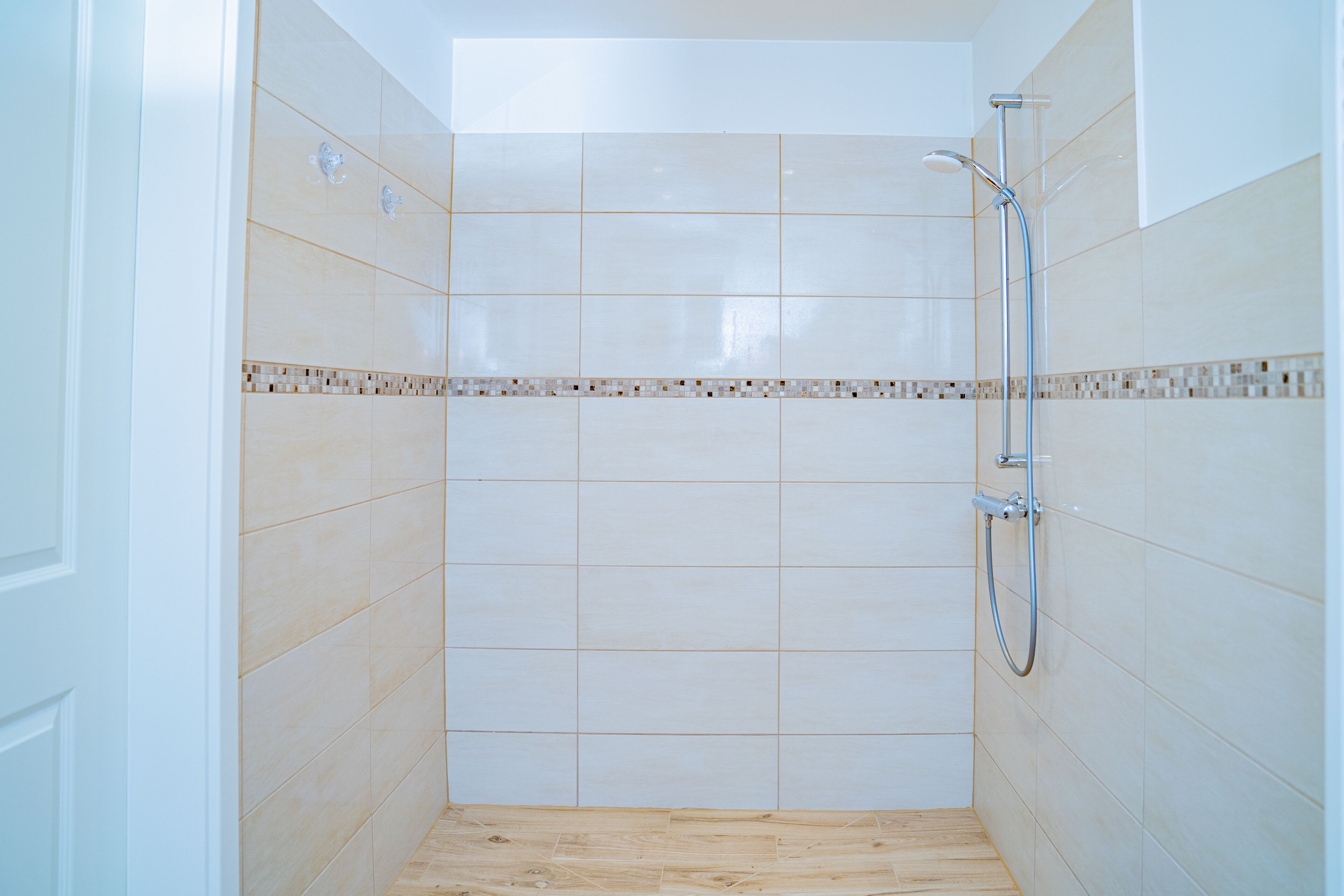 A small, tiled shower room with a wooden floor and a showerhead.