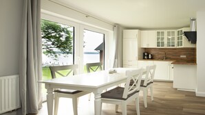 A dining area with a white table and chairs, a view of the outdoors, and a kitchen with white cabinets and a wooden countertop.
