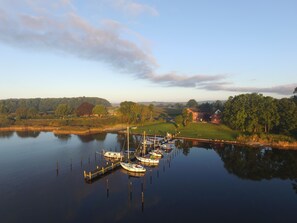 A calm lake with boats docked at a pier, surrounded by greenery and a few buildings. - Appartementhaus Schleiblick (Rabenkirchen-Faulueck)