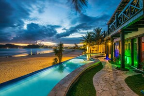 A pool area with a view of the beach and ocean, stone pathway, and a building with a balcony. - Chez Pitu Praia Hotel (Búzios)