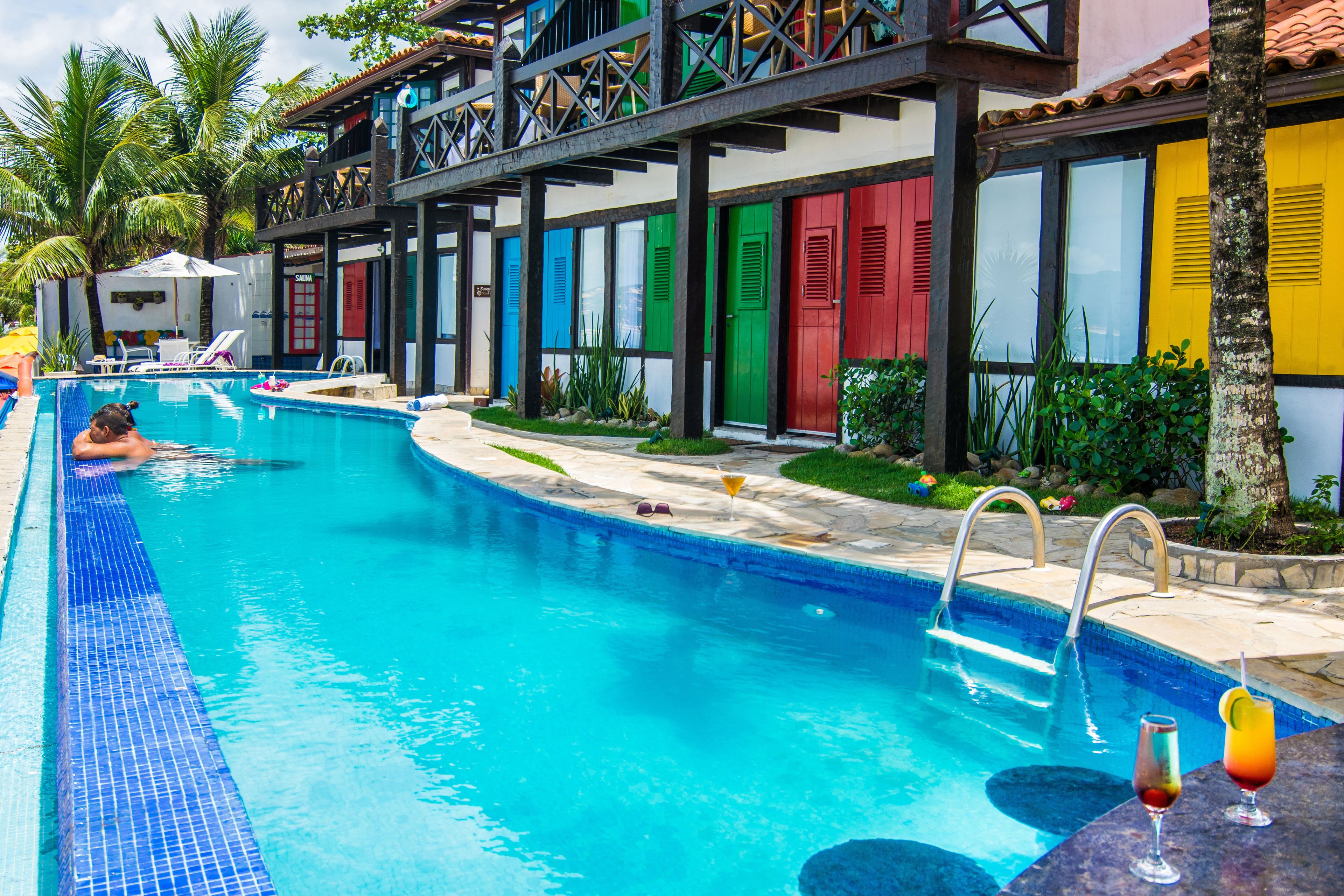 A swimming pool with a person in the water, a bar area with drinks, and colorful doors.