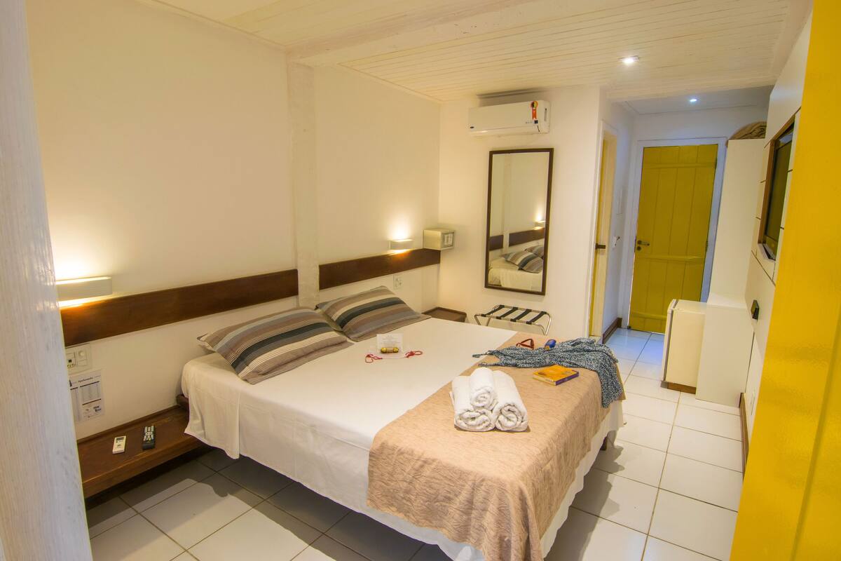 A hotel room with a bed, bedside table, lamp, and a mirror.