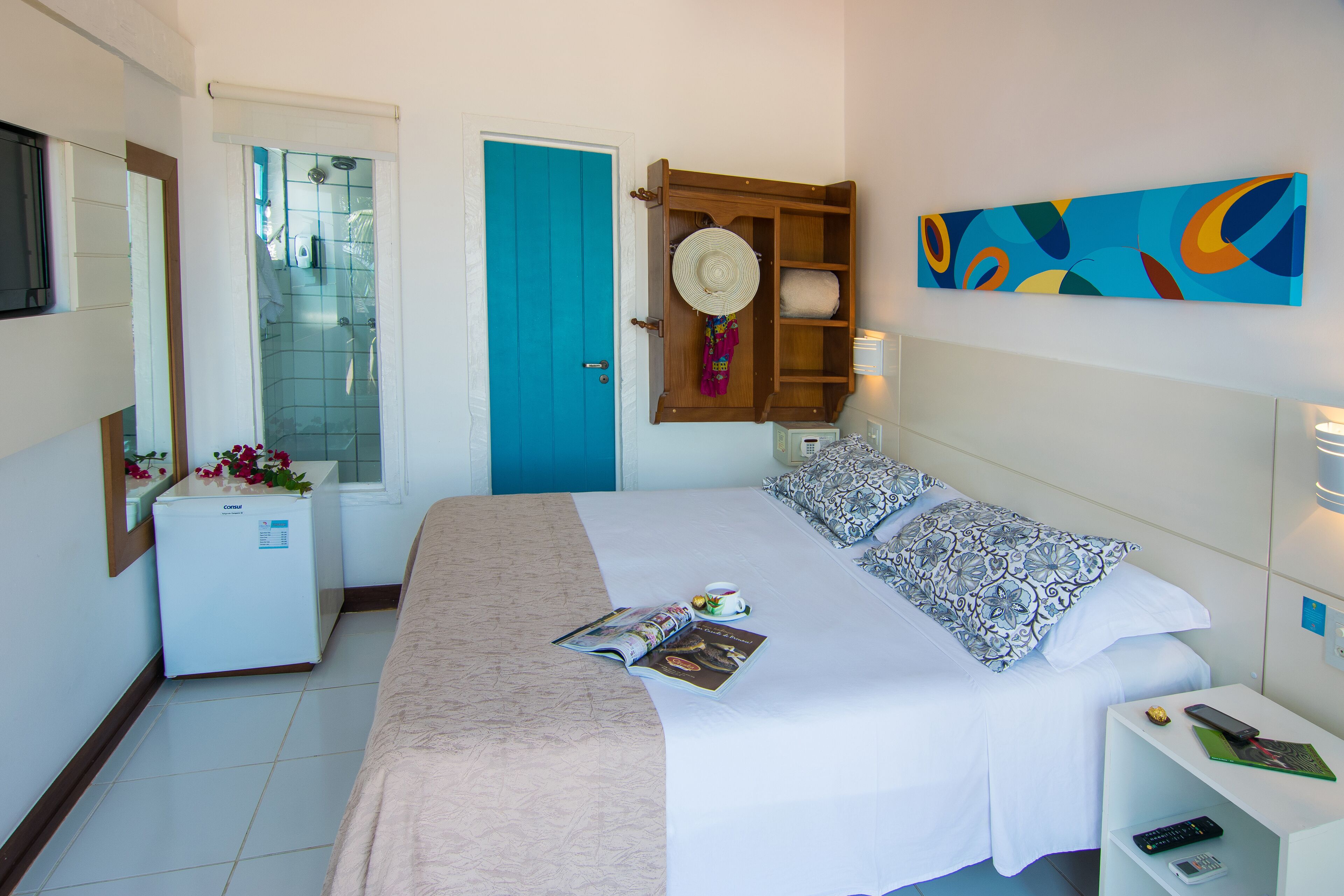 Una habitación de hotel con cama, mesita de noche, cuadro en la pared, puerta y ventana.